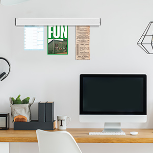 Minimalist home office setup with wooden desk, computer monitor, wall decorations, and small plants against a white wall.